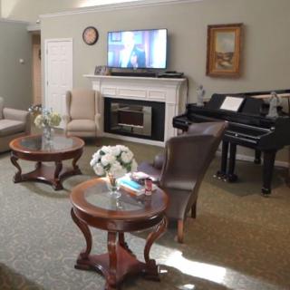 A cozy living room featuring a piano, coffee tables, and a TV over the fireplace.