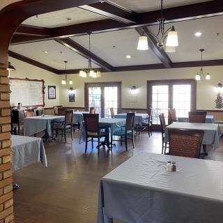 A spacious dining room with neatly arranged tables and chairs, featuring elegant lighting and wooden ceiling beams.