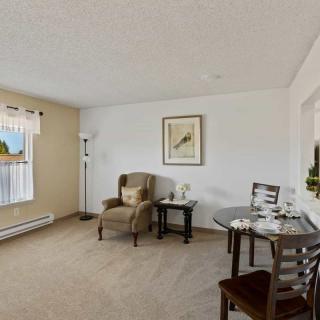A cozy living room with a comfortable chair, a small dining table set, and a window letting in natural light.