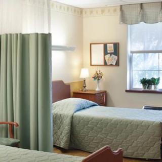 A hospital room with two beds, separated by a curtain, and a window letting in natural light.