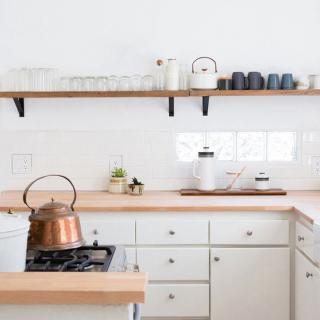 A minimalist kitchen featuring white cabinets, wooden countertops, and a copper kettle on the stove.
