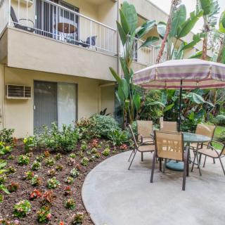 A cozy apartment patio with garden seating under a large umbrella surrounded by lush plants.