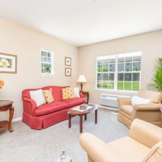 Bright and cozy living room with a red sofa, beige armchairs, and large windows.