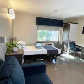 A modern apartment bedroom with sleek furnishings, featuring a bed, desk, and large window.