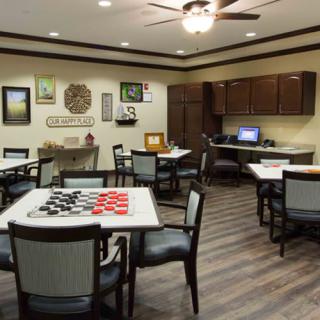 A cozy game room featuring tables with checkers, a computer desk, and wall art, all under a ceiling fan.