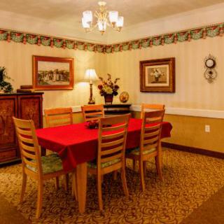 A cozy dining room with a wooden dining set adorned with a red tablecloth, surrounded by warm lighting and tasteful wall decor.