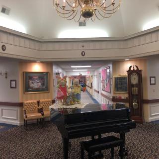A luxurious hallway with a grand piano, decorated with paintings and a chandelier.