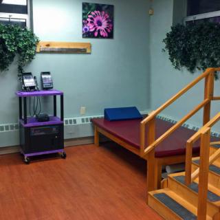 A physical therapy room featuring a therapy bed, wooden stairs for exercises, and indoor plants creating a calm atmosphere.