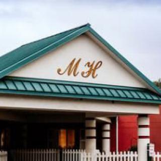A building entrance with a green roof and the initials 'MH' displayed prominently.