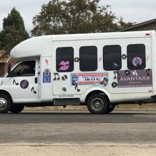 A white van with business advertisements and decorative stickers on the side is parked by the road.