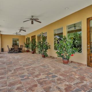 A spacious outdoor patio with tile flooring, ceiling fans, and potted plants.