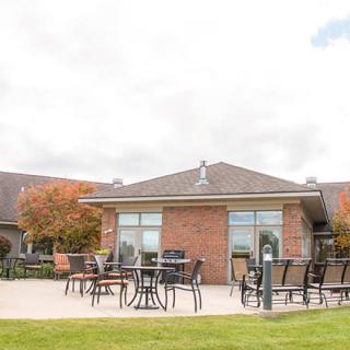 An outdoor patio area with tables and chairs in front of a brick building surrounded by autumn foliage.