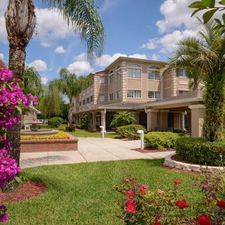 A scenic view of a building surrounded by lush gardens with palm trees and colorful flowers on a sunny day.
