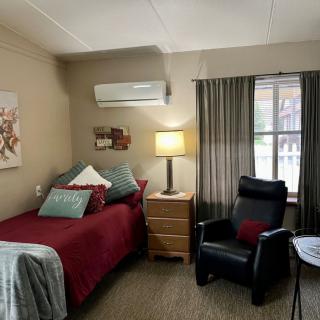 A cozy bedroom with a single bed, lamp, and comfortable chair by the window.