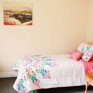 A cozy bedroom with a single bed featuring colorful bedding and a landscape painting on the wall.