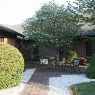 A tranquil patio with outdoor seating surrounded by lush greenery and a small tree.