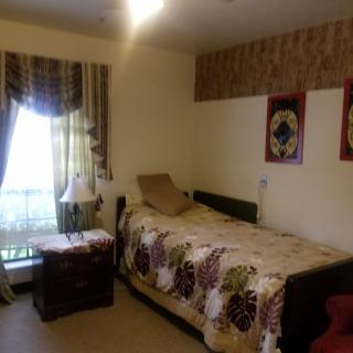 A cozy bedroom with a single bed, decorative quilt, and sunlight streaming through the window.