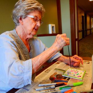An elderly woman engaged in painting as a creative hobby indoors.