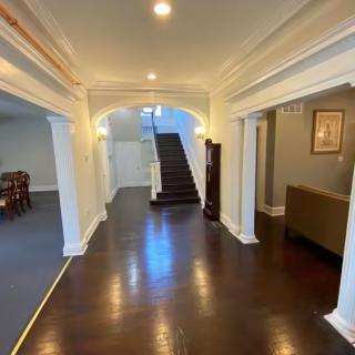 A spacious hallway with dark wood flooring and an archway leading to a staircase.