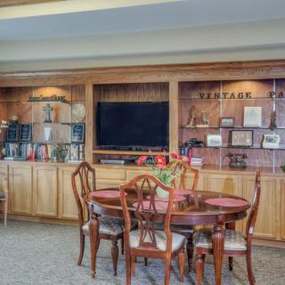 A cozy living room with wooden furniture, featuring a dining table and a television on wooden shelves adorned with decorative items.