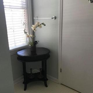 A dark round table with a vase of flowers in a bright corner near a window and door.