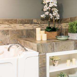 A cozy bathroom with decorative candles, plants, and stylish tiles surrounding the bathtub.