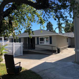 A small residential house with a driveway and surrounding trees on a sunny day.