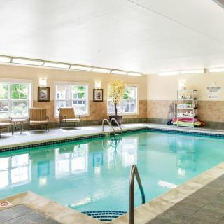 A well-lit indoor swimming pool area with seating and towel rack.