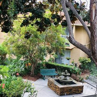 A peaceful garden setting with a central fountain, surrounded by lush trees and greenery, accompanied by a bench for relaxation.