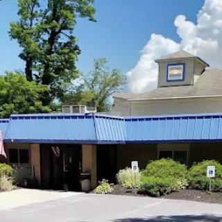 A charming hotel with a blue roof surrounded by lush greenery and under a clear sky.