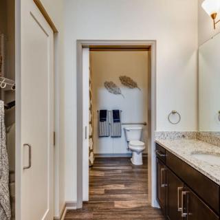 A modern bathroom with a view of the toilet area, featuring a wide countertop with a sink and mirror.
