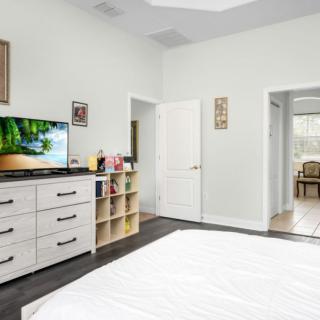 A modern and minimalist bedroom featuring a dresser with a TV, simple decor, and an open doorway leading to another room.