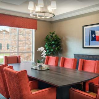 A modern dining room with red chairs and a rectangular table, decorated with an indoor plant and artwork.