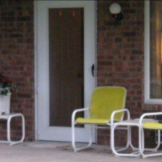 A cozy porch area with yellow metal chairs and a small table near a brick wall.