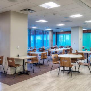 An empty cafeteria with tables and chairs arranged neatly under bright lighting.