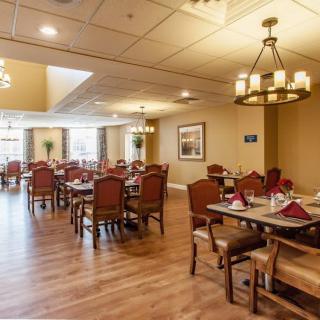 A spacious dining room with elegant chandeliers, neatly arranged tables and chairs, and a warm wooden floor.