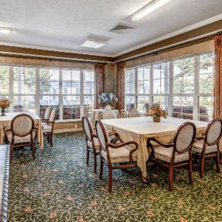 A well-lit dining area with multiple tables and chairs arranged neatly, surrounded by large windows.
