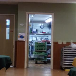 A glimpse into a commercial kitchen through an open doorway, showcasing storage racks and kitchen equipment.