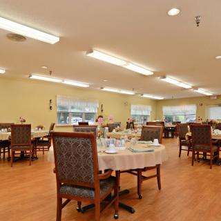A spacious dining area with neatly arranged tables and chairs, featuring warm lighting and a wooden floor.