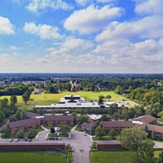 Aerial view of a campus surrounded by greenery under a partly cloudy sky.
