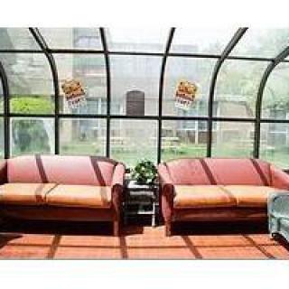 A sunlit room with two sofas and a glass ceiling, featuring indoor plants and ample natural light.
