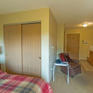 A cozy bedroom with a plaid bedspread, wooden closet doors, and comfortable seating.