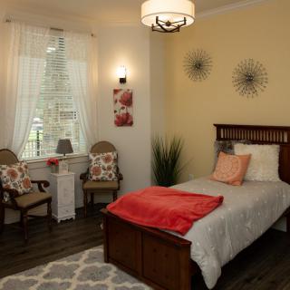 A cozy bedroom with modern decor features a single bed, decorative pillows, and natural lighting from the window.
