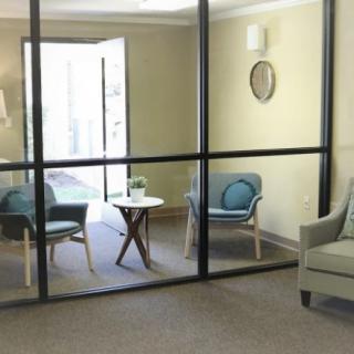 A cozy office waiting area with soft chairs and a small table, partitioned by glass walls.