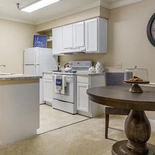 A modern kitchen with white cabinets and appliances, including a fridge and stove, adjacent to a dining table.