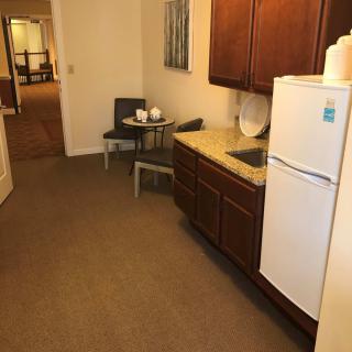 A small kitchen area in an apartment with a refrigerator, cabinets, and a dining table with chairs.