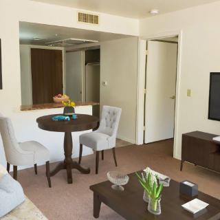 A cozy living room with minimalist decor, featuring a small dining table, TV, and fresh flowers.