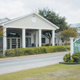 A building entrance with white columns and a green sign surrounded by neatly trimmed bushes.