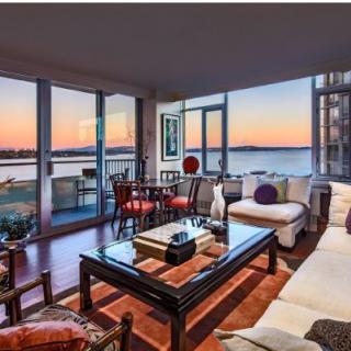 A modern living room with panoramic ocean and sunset views through large glass windows.
