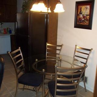 A dining area featuring a glass-top table with four metal chairs and a decorative chandelier, complemented by wall art.